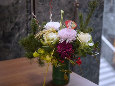 お花畑の上を鶴が舞っているプルモサムとケイトウのお正月しめ縄